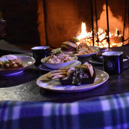 A cozy dining setup with various dishes and mugs, set against a warm fireplace backdrop.