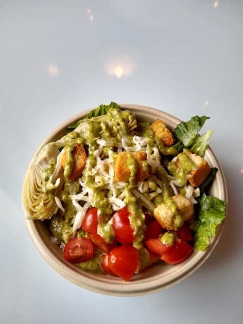A bowl of salad with lettuce, cherry tomatoes, croutons, artichokes, and a green dressing.