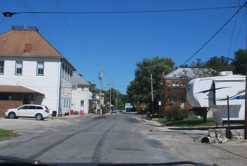 A view of a quiet street with buildings, parked cars, and a stop sign under a clear blue sky.
