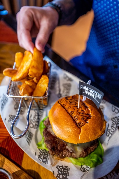 A close-up of a high-octane burger with lettuce and a side of crispy potato wedges on a plate.