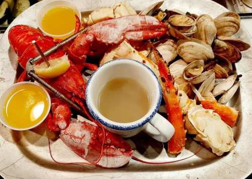 A seafood platter featuring lobster, crab, clams, and dipping sauces on a metal tray.