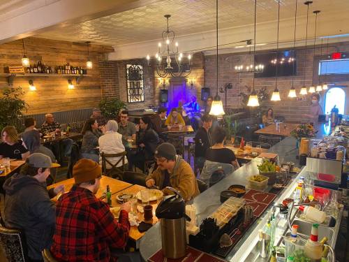 A lively restaurant scene with diners enjoying meals and drinks, surrounded by warm lighting and rustic decor.
