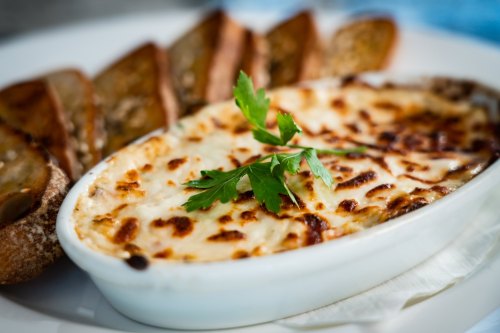 A creamy baked dish topped with golden cheese, served with toasted bread slices and garnished with a sprig of parsley.