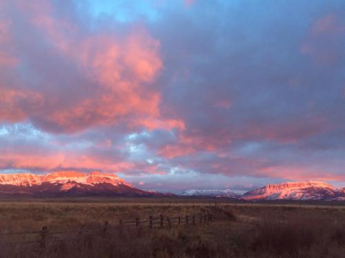 Sunset over snow-capped mountains, with vibrant pink and orange clouds illuminating the sky and a grassy foreground.