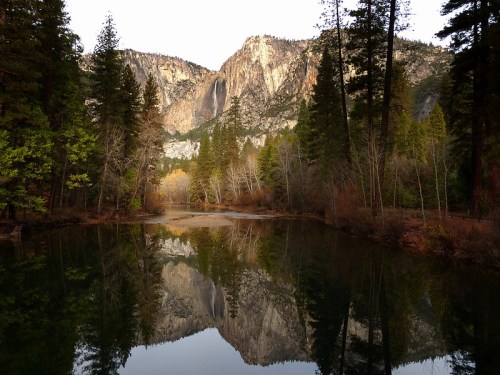 A serene lake reflects towering mountains and lush trees in a tranquil natural setting.