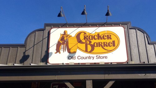 Sign for Cracker Barrel Old Country Store featuring a logo with a man sitting on a barrel against a blue sky.