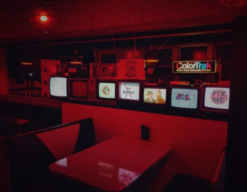 A dimly lit diner with multiple vintage TVs displaying static and text, creating a retro atmosphere.