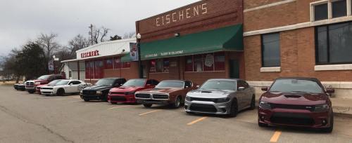 A row of eight cars parked in front of a building with a sign that reads "Eischens," showcasing various models and colors.