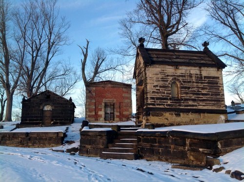 Three historic mausoleums in a snowy landscape, surrounded by bare trees under a clear blue sky.