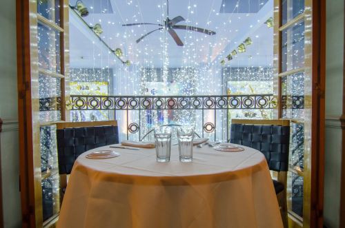A cozy dining table set for two, with glasses, in a beautifully decorated room with twinkling lights.