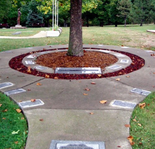 A circular pathway around a tree, featuring plaques and decorative mulch in a park-like setting.