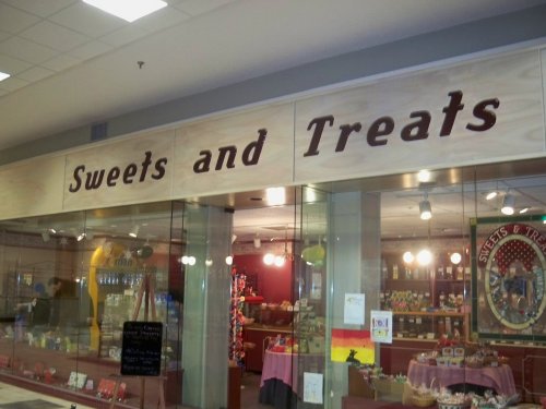 Sign for "Sweets and Treats" shop with colorful displays of candies and treats visible through the glass storefront.