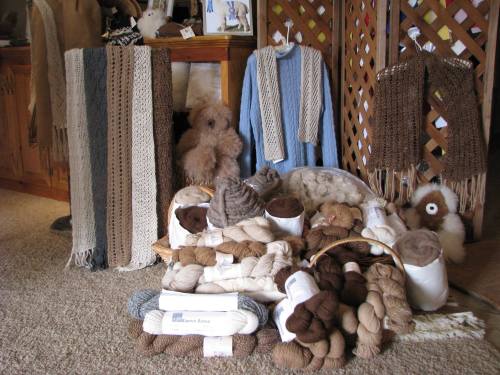 A cozy display of handmade scarves and various yarns in neutral tones, with a few plush toys in the background.