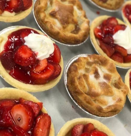 A variety of mini fruit tarts and pies, featuring strawberries and whipped cream, arranged on a tray.