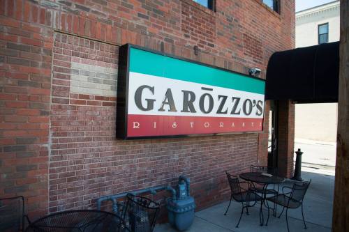 Sign for Garozzo's Ristorante on a brick wall, with outdoor seating visible in front.