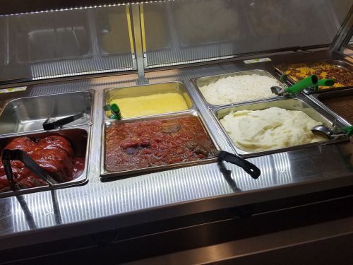 A buffet display with various dishes, including meat, rice, mashed potatoes, and cornbread, in metal trays.