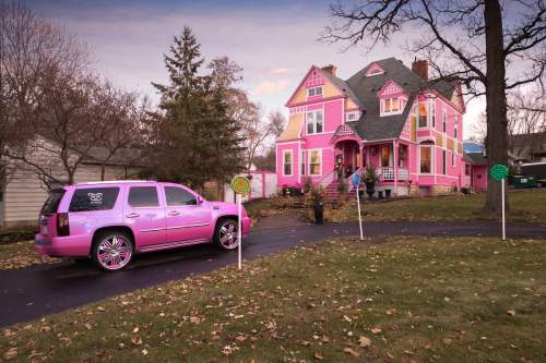 A bright pink house with a matching pink SUV parked outside, surrounded by autumn leaves and whimsical lollipop decorations.