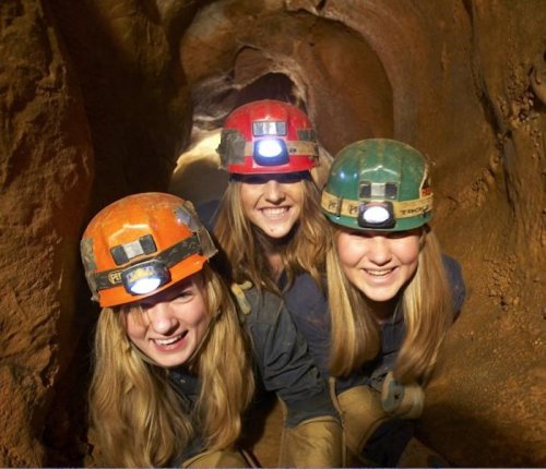 Three smiling individuals in helmets with headlamps, posing inside a cave tunnel.