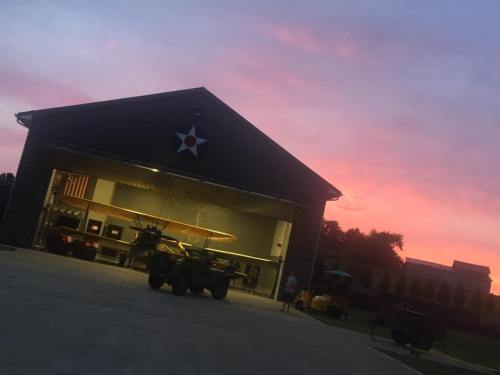 A garage with a vintage airplane inside, set against a colorful sunset sky.