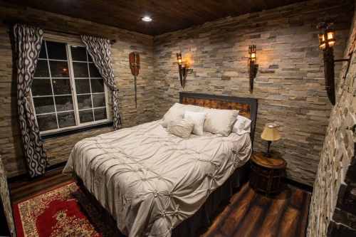 Cozy bedroom with stone walls, a large bed, decorative lighting, and a window with curtains.