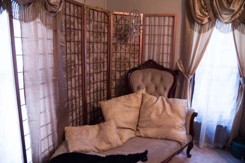 A cozy sitting area featuring an ornate couch with decorative pillows, a folding screen, and elegant curtains.