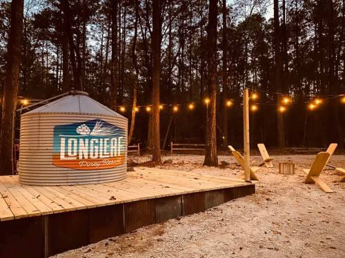 A rustic outdoor area with a metal structure, string lights, and wooden seating in a forested setting at dusk.