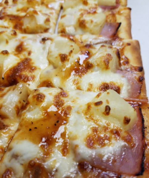Close-up of a cheesy pizza topped with ham and pineapple, featuring a golden, bubbly crust.