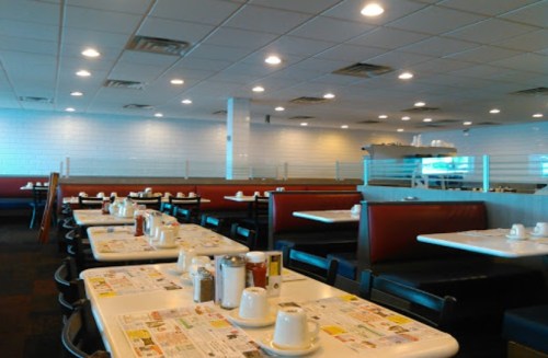 A spacious diner interior with empty tables, white walls, and bright lighting, featuring condiments and menus on tables.