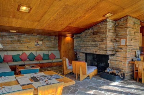 Cozy living room with a stone fireplace, wooden ceiling, and colorful cushions on a sofa, featuring a rustic design.