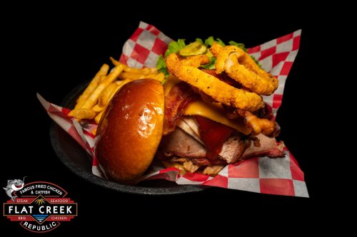A delicious burger with cheese, bacon, and onion rings, served with fries in a basket with a checkered liner.