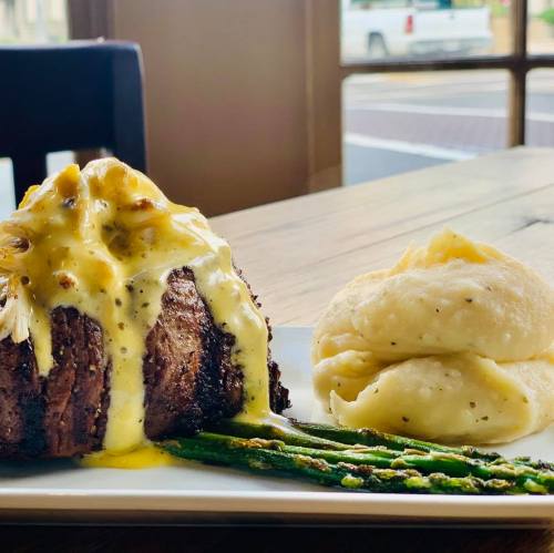 A plated meal featuring a steak topped with sauce, asparagus, and creamy mashed potatoes on a wooden table.