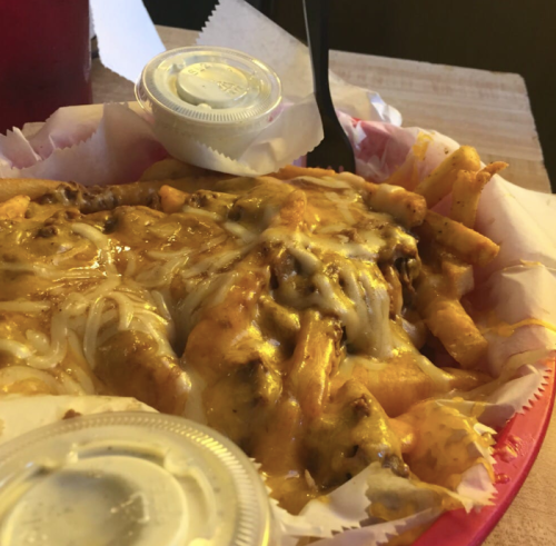 A close-up of a basket of cheesy chili fries with two small containers of sauce on the side.
