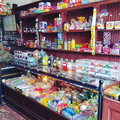 A colorful candy shop display with jars and boxes of various sweets and treats on wooden shelves.