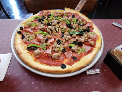 A large pizza topped with pepperoni, sausage, green peppers, and black olives on a silver tray.