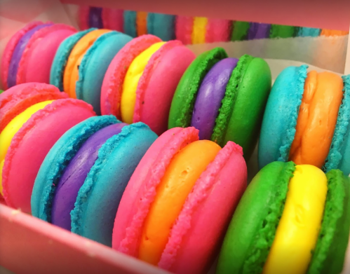 A colorful assortment of macarons in pink, blue, green, orange, and purple, neatly arranged in a box.