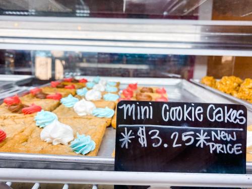 A display of mini cookie cakes with colorful frosting, priced at $3.25, in a bakery case.