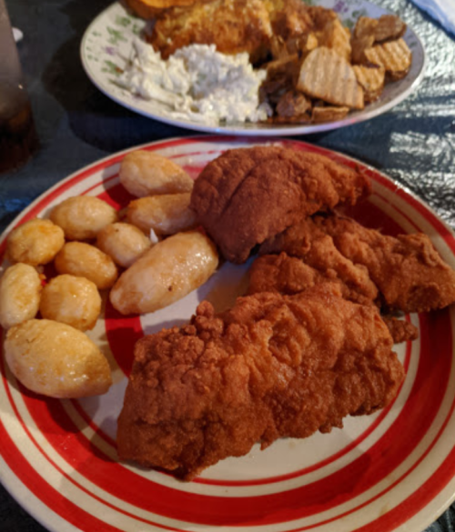 A plate of fried chicken, golden potato dumplings, and a side of crispy chips.