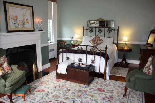 Cozy bedroom with a vintage bed, floral decor, a fireplace, and a patterned rug, creating a warm, inviting atmosphere.