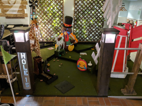 A whimsical mini-golf hole featuring a colorful character, animals, and playful decorations in a vibrant setting.