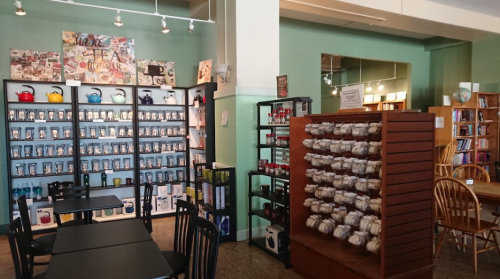 A cozy shop interior with shelves of tea and coffee products, wooden tables, and a warm, inviting atmosphere.