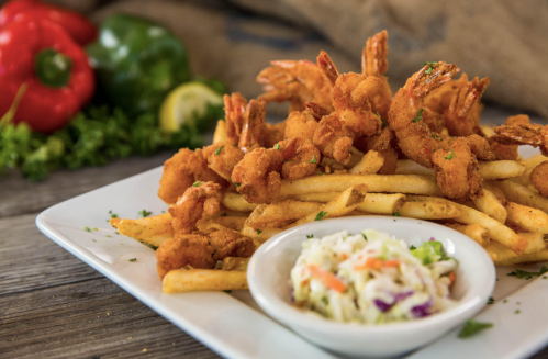 A plate of crispy fried shrimp served over golden fries, accompanied by a side of coleslaw and fresh vegetables.