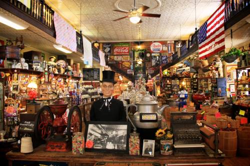 A vintage store interior filled with antiques, a mannequin in a top hat, and colorful decorations.