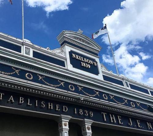 Historic building facade with "Neilson's 1839" and "Established 1839" signs under a blue sky with clouds.
