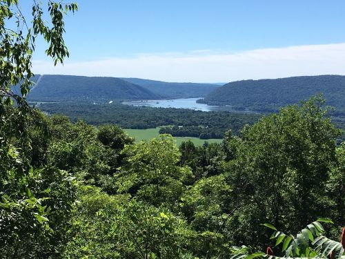 A scenic view of a river winding through green hills and trees under a clear blue sky.