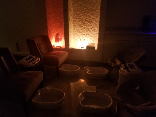 A dimly lit spa room with chairs and foot baths, featuring glowing salt lamps and a serene atmosphere.