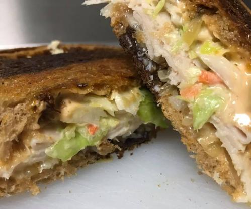 Close-up of a toasted sandwich, revealing layers of chicken, lettuce, and a creamy spread inside.