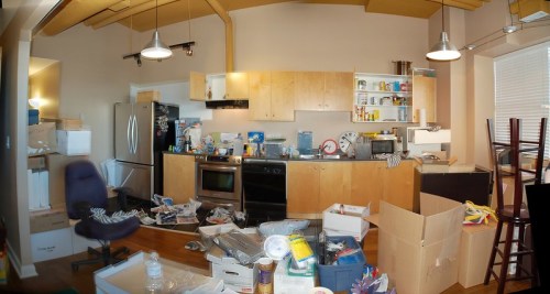 A cluttered kitchen with boxes, scattered items, and a messy countertop, showcasing disorganization and chaos.