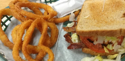 A plate with a sandwich filled with lettuce and tomato, alongside a serving of crispy onion rings.