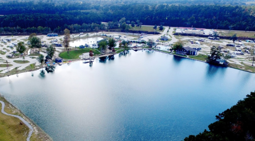 Aerial view of a serene lake surrounded by trees and a campground with recreational facilities.