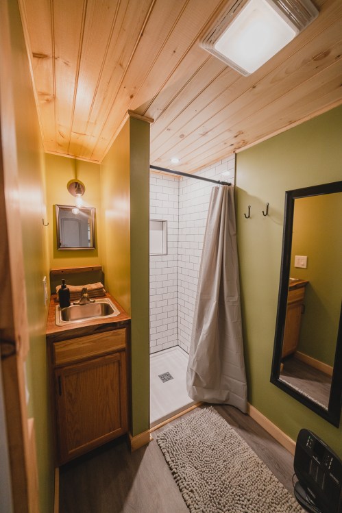 A small bathroom featuring a sink, shower with curtain, and wooden accents, with green walls and a mirror.